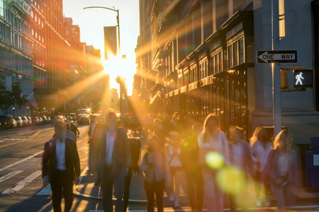 Crowd of blurred people crossing a busy intersection on 5th Avenue in New York City with the bright light of sunset in the backgroundの写真素材