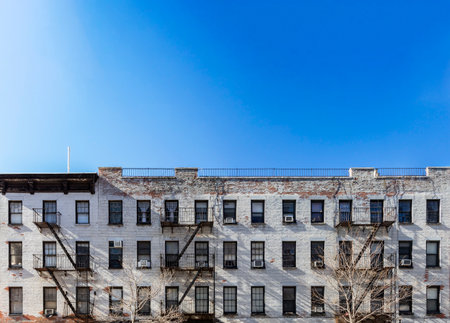 Panoramic view old white brick apartment building with windows and fire escapes and an empty blue sky background overhead in New York City NYCの写真素材