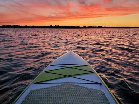 Paddleboard floating on the water with the colorful light of sunset reflecting off the waves of a lake at duskの写真素材
