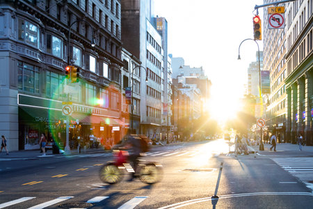 New York City - A delivery person on a bike rides through the busy intersection on 14th Street and 5th Avenue in Manhattan with the sun setting in the backgroundのeditorial素材