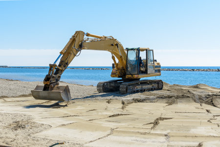 excavator that is working on the beach to smooth the sand before the start of the summer season