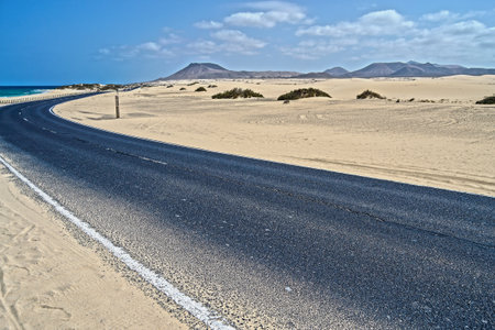 typical asphalted street in the desert, surrounded by white beach and dunes, Corralejo, Fuerteventura, Canary Islands, Spainの写真素材