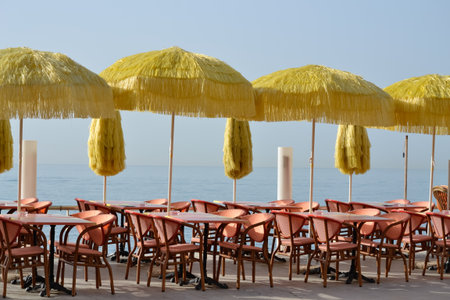 Bar tables, chairs and beach umbrellas, along the seashore, in the blue coast, Menton, Franceの写真素材