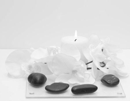 White candle with flame, black rocks, and white flowerの写真素材