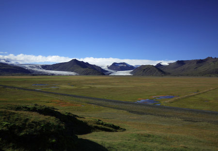 Icelandic Glacier over green fields against a blue skyの写真素材