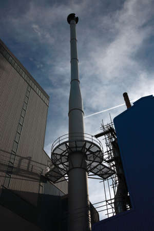 Industrial chimney silhouetted against the blue cloudy skyの写真素材