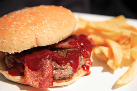 Juicy burger with bacon and fries on a white plateの写真素材