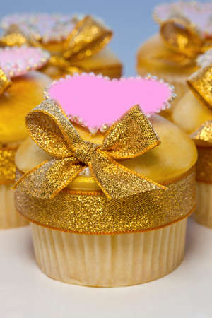 Iced cup cakes decorated with golden bows and pink hearts の写真素材