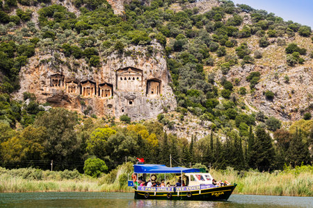 DALYAN, TURKEY - 16 APRIL 2018:  River boat with tourists on the river Dalyan by the sheer cliffs with the weathered facades of Lycian tombs cut from rock, circa 400 BC.のeditorial素材