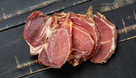 Dried lamb jerky slices on wooden board with salt and pepperの写真素材