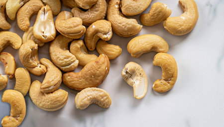 A pile of roasted cashew nuts scattered on a white marble backgroundの写真素材
