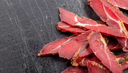 Dark banner of sujuk flat cured sausage. Sausage cut from dry meat on a wooden Board with herbs and...