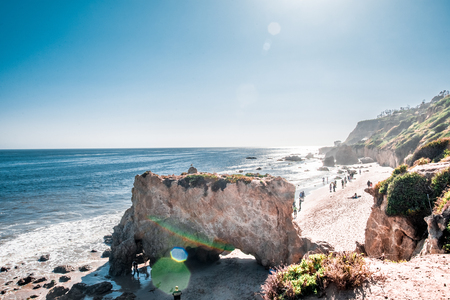 People walking along a rocky beach with a blue skyの写真素材