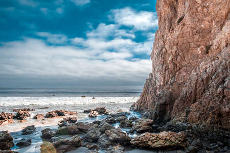 Rocky beach by a cliff with a blue cloudy skyの写真素材