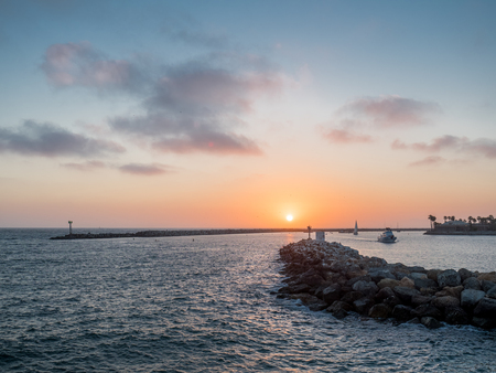 Red sky with sun setting behind breakwaterの写真素材