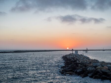Red sky with sun setting behind breakwaterの写真素材