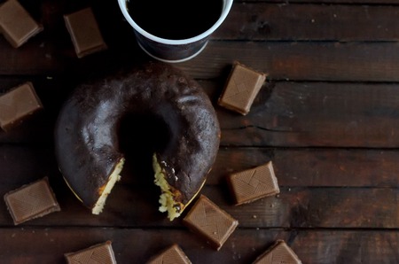 Bitten chocolate donut with coffee and milk chocolate on wooden background.Sweet dessert in the morning.Copyspace right.の写真素材