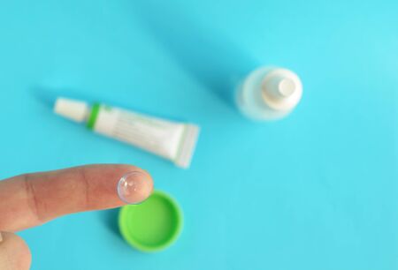 Contact lens on forefinger on light blue background.Eye care products in the background, space for text ,top view.の写真素材