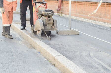 Road worker cutting asphalt road, working on the road reconstruction.の写真素材