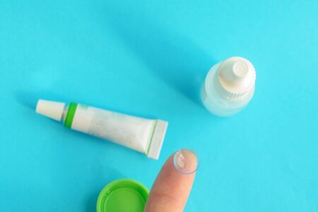 Contact lens on finger, tube of eye ointment and small bottle of eye drops on light blue background..Top view.の写真素材