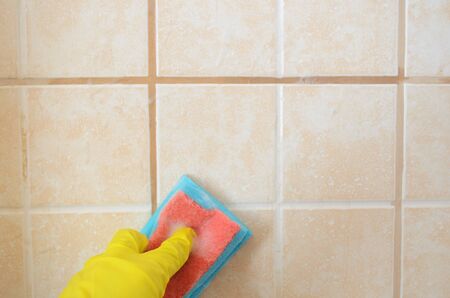 hand in yellow protective glove with sponge washes ceramic tiles with washing foam . Early spring cleaning or regular clean up.Space for text on topの写真素材