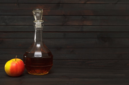 A decanter with apple cider vinegar and whole red yellow apple on dark wooden background.の写真素材