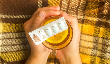 Top view on man hands holding a glass of hot tea with lemon and pills.の写真素材
