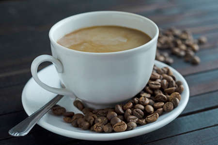 a cup of coffee with cream and coffee beans on a saucer.の写真素材
