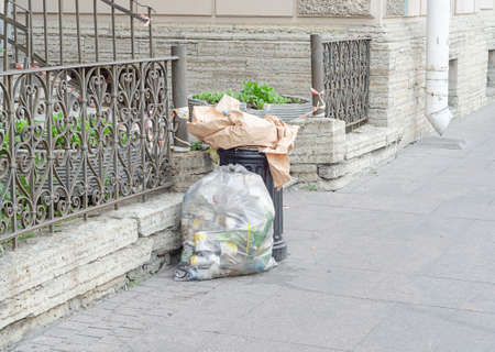 overflowing garbage litter bin and full plastic package with garbage in the street.