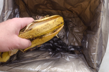 a man puts banana skins into garbage trash.Waste food conceptの写真素材