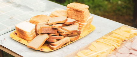 Tray with slices of white and black bread, slices of cheese and bacon on table for summer sandwiches