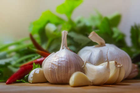 garlic bulb is surrounded by green leafy vegetables and chilies on a wooden chopping board.の写真素材