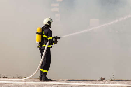 Firefighter in protective suit works with water hose. Fighting for a fire attackの写真素材
