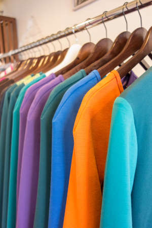 Line of multi colored clothes on wooden hangers in store. Sale