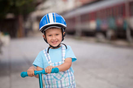 happy little boy with helmet, playing with his scooter outdoorの写真素材