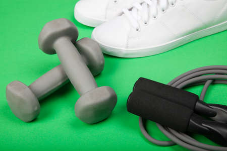 Sport shoes, dumbbells and skipping rope on green background. Fitness, sport and healthy lifestyle concept.の写真素材