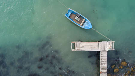 Lonely fishing boat and wooden pier in turquoise ocean, sea. Aerial photo, top viewの写真素材