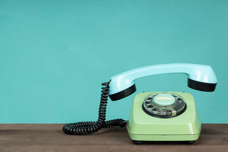 Old telephone on wooden table in front of green background. Vintage phone with taken off receiver. Vintage style photo. の写真素材