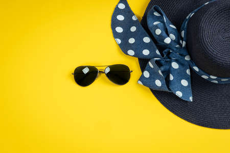 Blue hat with ribbon and sunglasses on yellow background. Summer concept. Top view with copy spaceの写真素材