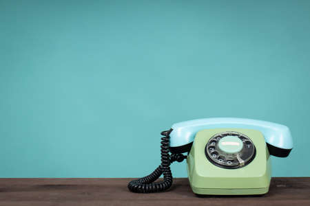 Old telephone on wooden table in front of green background. Vintage phone