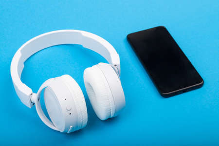 Smartphone mobile phone with wireless white headphones on blue background. Ready to listen to music.の写真素材