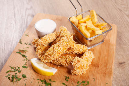Corn flakes deep fried chicken sticks andfrench fries, served on wooden board