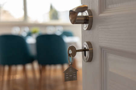 Open door to a new home. Door handle with key and home shaped keychain. Mortgage, investment, real...