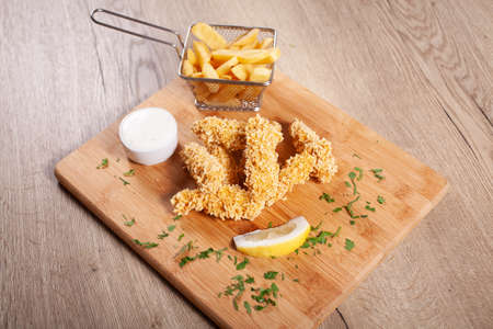 Corn flakes deep fried chicken sticks andfrench fries, served on wooden boardの写真素材