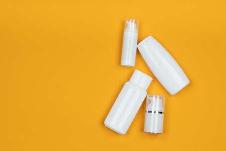 White jars and containers of cosmetics on yellow background. Skincare product set. Face and body...