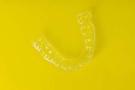 Invisible orthodontics cosmetic brackets on yellow background. Tooth aligners, for beautiful smile.