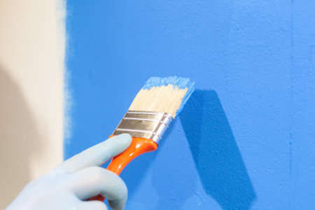 Close up of male hand in gloves painting a wall with blue paint. Repair and home renovation conceptの写真素材
