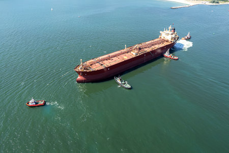 Aerial view of tug boat assisting big oil tanker. Large oil tanker ship enters the port escorted by tugboats.の写真素材