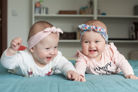 Adorable baby twins having fun in bed at home. Cute kids with hairbands (ribbons), smiling, laughing. Happiness concept.の写真素材