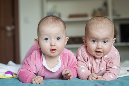 Adorable six months old baby twins in bed at home. Cute kids during tummy time. Two baby twins on bed.の写真素材